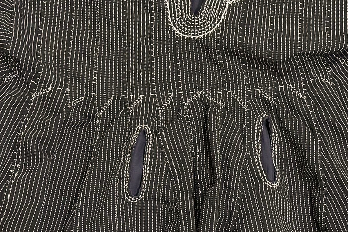 Near-black ground with white warp pinstripe and weft dashes on a hand-woven Black & White fugu smock, pattern stepping across the strip seams